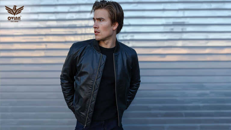A man wearing a black leather bomber jacket with a quilted pattern on the shoulders, standing in front of a metal background.