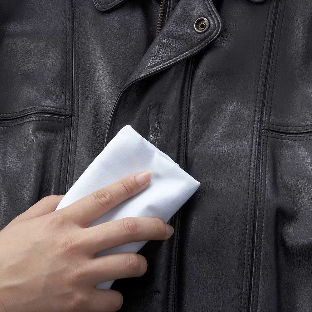 Hand cleaning a black leather jacket with a white cloth.
