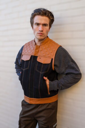 Model wearing the OVLAN denim and leather motorcycle vest, showcasing a unique design with tan leather details, quilted shoulders, and durable denim fabric.
