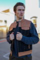 Model wearing an OVLAN denim and leather motorcycle vest featuring quilted tan shoulders, black denim panels, and brown leather accents, posing outdoors.