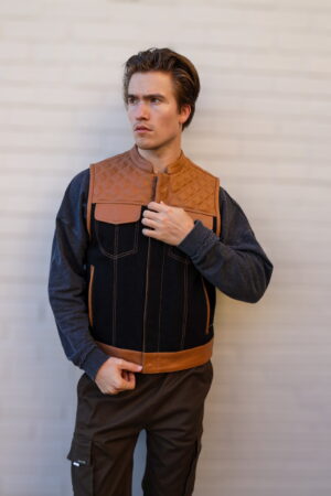 Model showcasing the OVLAN denim and leather motorcycle vest, featuring quilted tan shoulders, black denim body, and brown leather accents for a stylish biker look.
