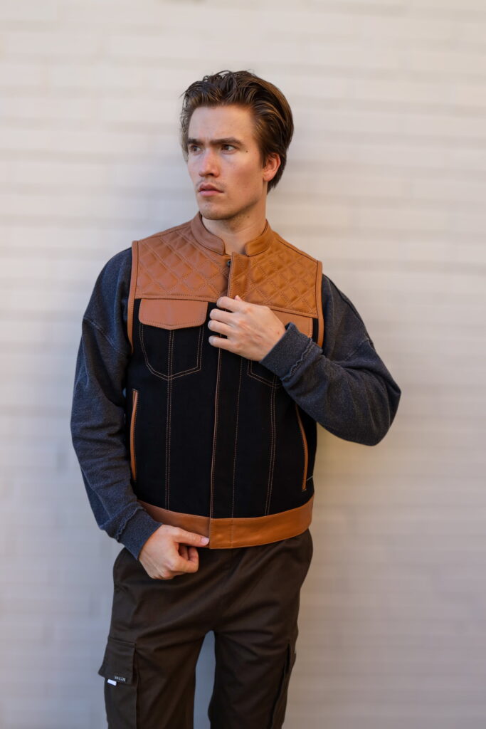 Model showcasing the OVLAN denim and leather motorcycle vest, featuring quilted tan shoulders, black denim body, and brown leather accents for a stylish biker look.