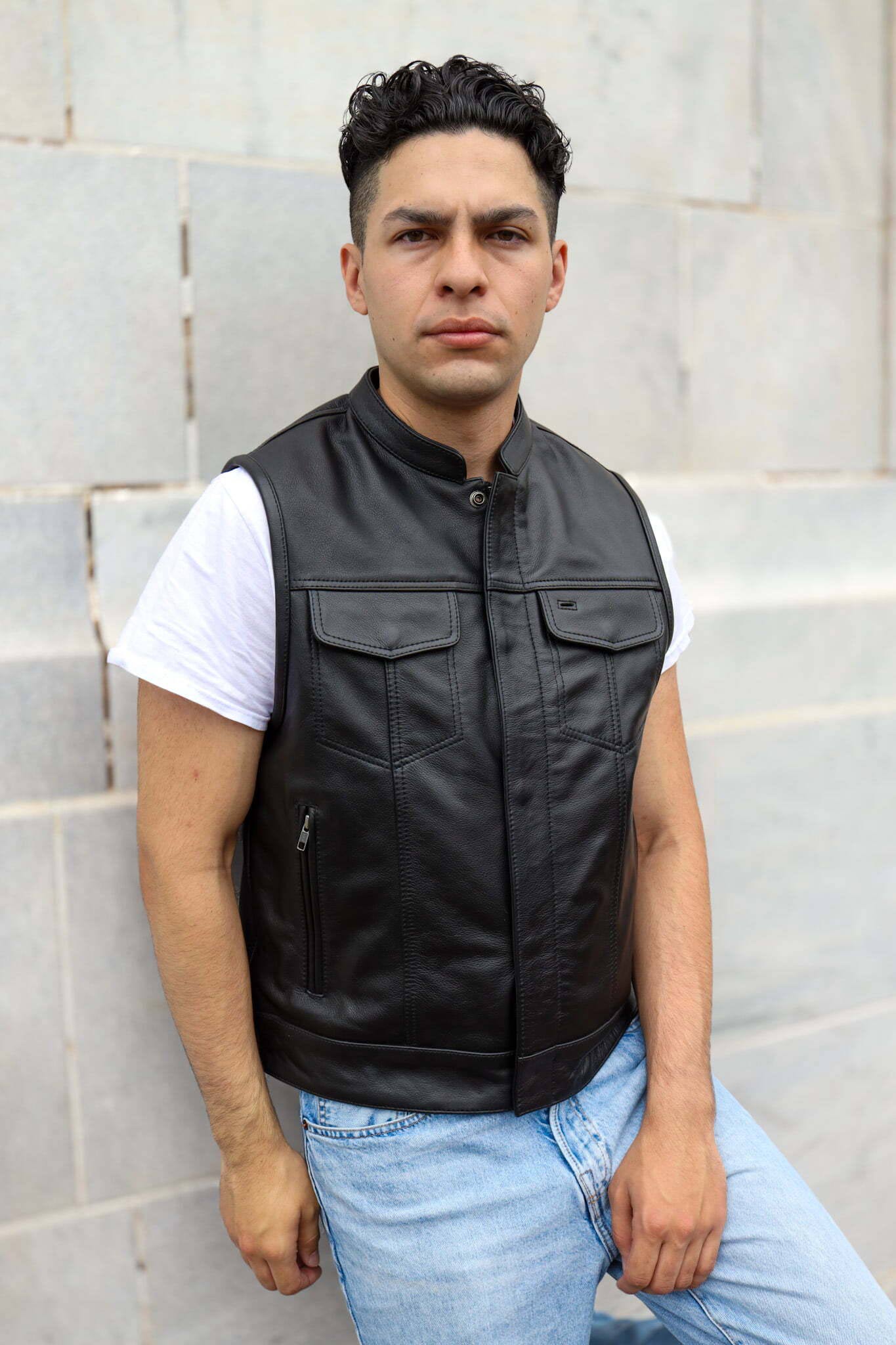 Man wearing a black leather vest, standing confidently.