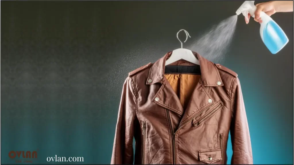 A brown leather jacket hanging on a hanger with a hand spraying it with a blue liquid.