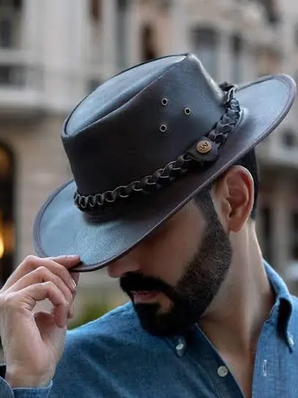 A man tipping his leather hat while wearing a blue shirt with a beard.