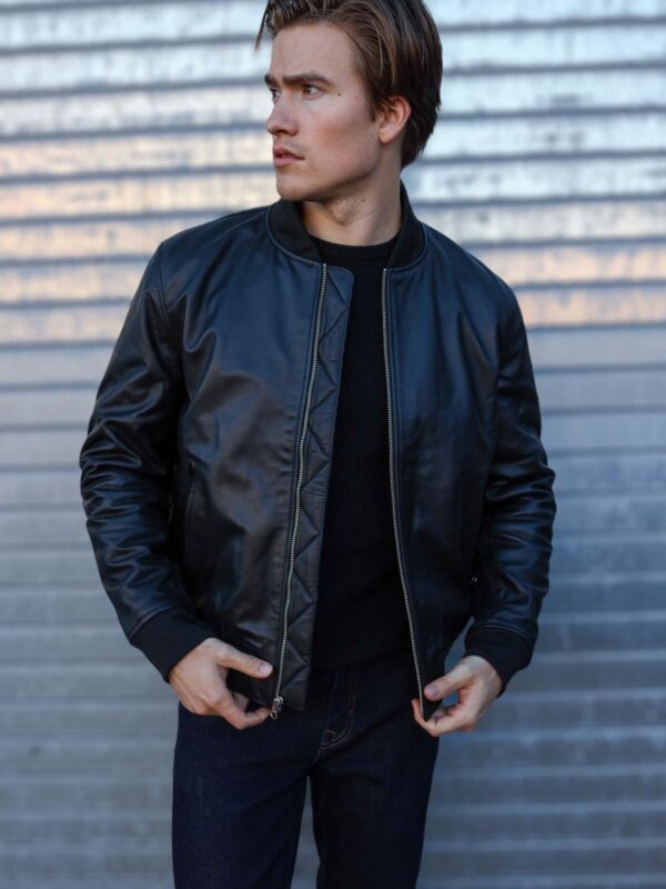 Person wearing a black bomber jacket in front of a metal background.