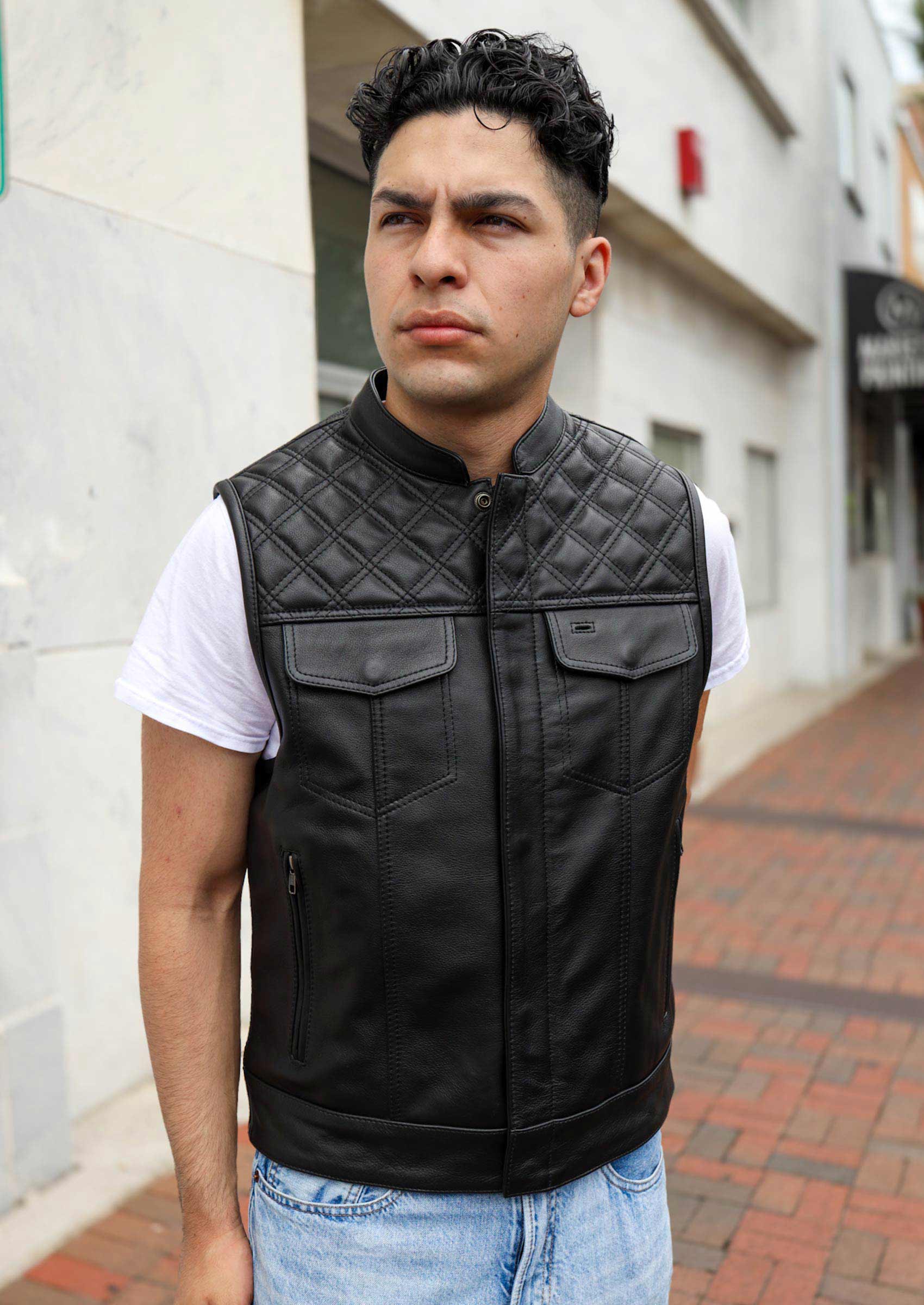 A man models a black leather motorcycle vest with diamond-stitched detailing, standing on a city sidewalk, showcasing its stylish and functional design.